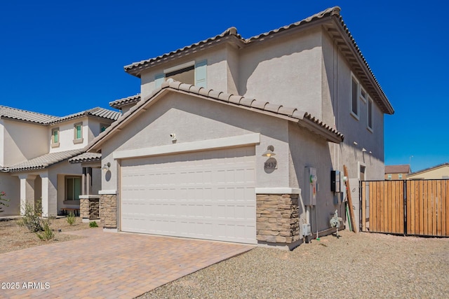 mediterranean / spanish-style home with decorative driveway, stone siding, an attached garage, and stucco siding