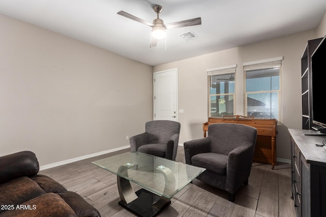 living area featuring a ceiling fan, visible vents, baseboards, and wood finished floors