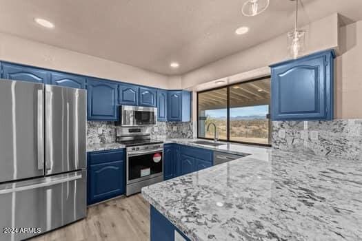 kitchen with tasteful backsplash, stainless steel appliances, light stone countertops, light hardwood / wood-style floors, and blue cabinets