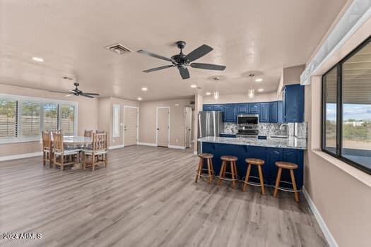 kitchen with kitchen peninsula, appliances with stainless steel finishes, a kitchen breakfast bar, light hardwood / wood-style flooring, and blue cabinets