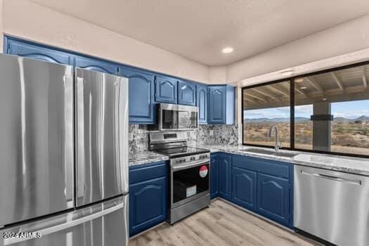 kitchen with stainless steel appliances, sink, backsplash, blue cabinetry, and light hardwood / wood-style flooring