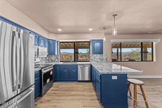 kitchen featuring stainless steel appliances, a breakfast bar, kitchen peninsula, backsplash, and blue cabinetry