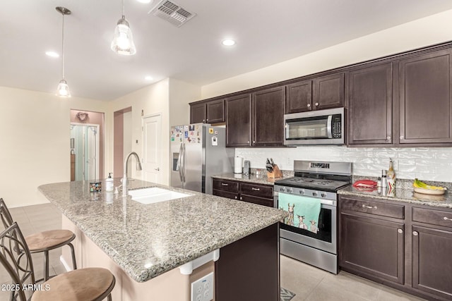 kitchen featuring visible vents, a kitchen bar, a sink, backsplash, and appliances with stainless steel finishes