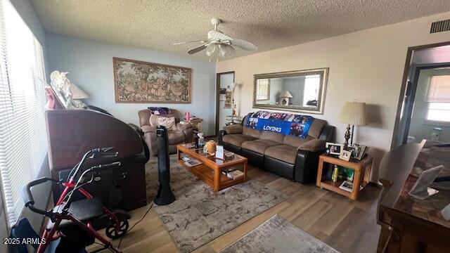 living room with wood finished floors, visible vents, a ceiling fan, and plenty of natural light