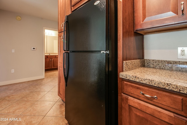 kitchen with light tile patterned flooring, black fridge, and light stone counters