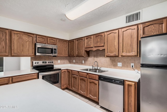 kitchen featuring stainless steel appliances, tasteful backsplash, light countertops, visible vents, and a sink