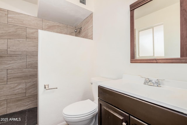 full bath with vanity, a tile shower, and toilet