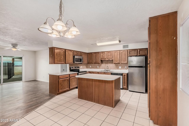 kitchen featuring brown cabinets, light tile patterned floors, stainless steel appliances, light countertops, and a sink