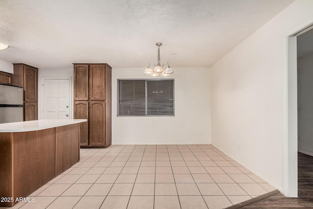 kitchen featuring freestanding refrigerator, hanging light fixtures, light countertops, a textured ceiling, and a notable chandelier