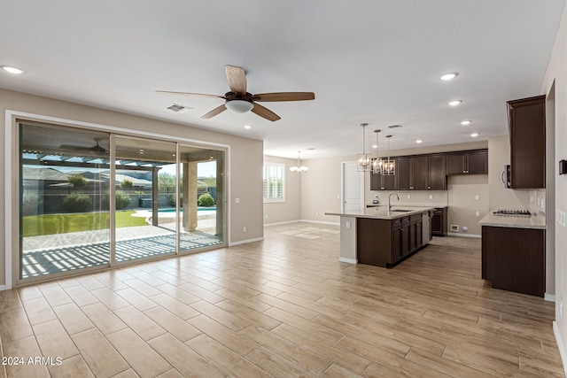 kitchen with sink, light wood-type flooring, dark brown cabinetry, decorative light fixtures, and a kitchen island with sink