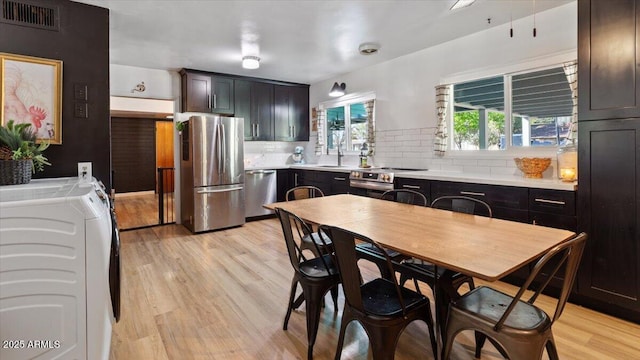 kitchen with light wood-type flooring, appliances with stainless steel finishes, light countertops, and washing machine and clothes dryer