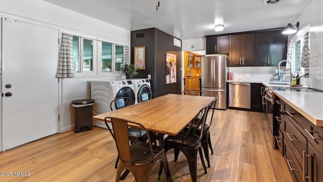 kitchen featuring a sink, appliances with stainless steel finishes, light wood finished floors, and washing machine and dryer