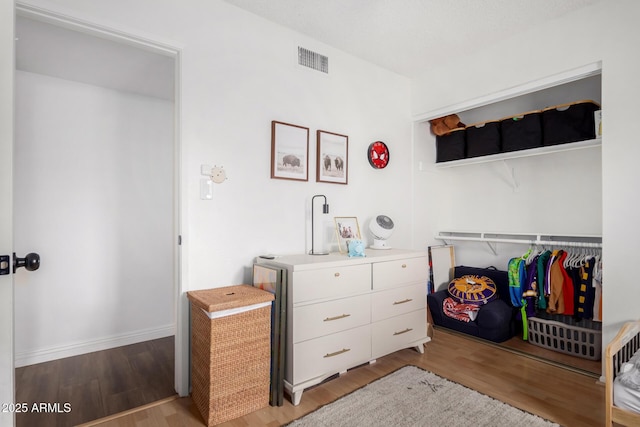 bedroom with wood finished floors, visible vents, a closet, and baseboards