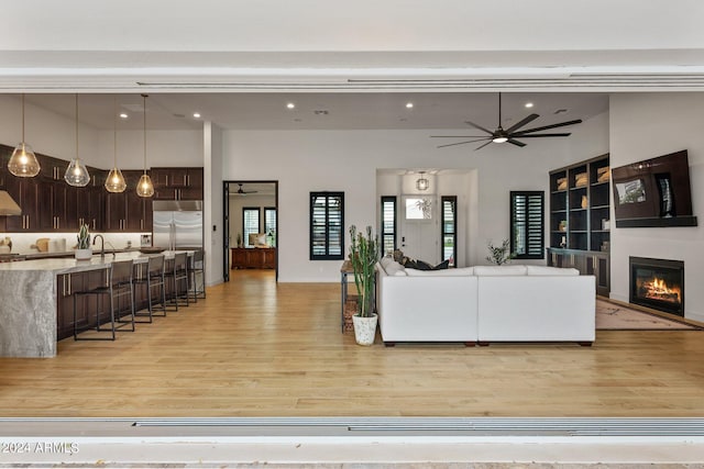 living area with light wood-style floors, a glass covered fireplace, ceiling fan, and a towering ceiling