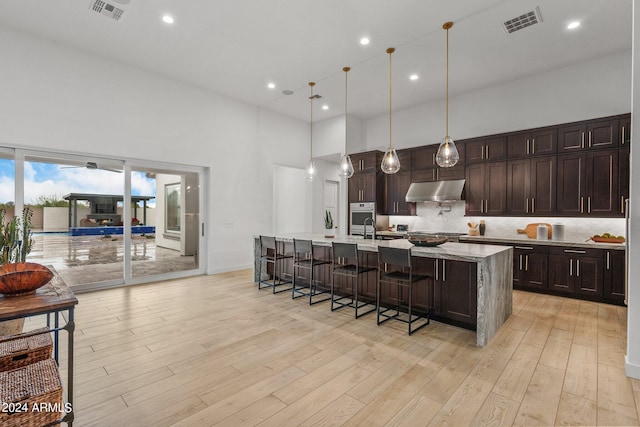 kitchen with under cabinet range hood, a towering ceiling, light wood-style floors, visible vents, and tasteful backsplash