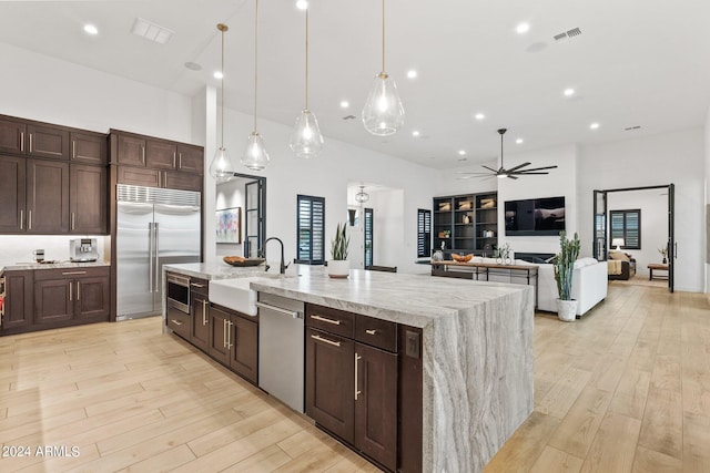 kitchen with a center island with sink, visible vents, built in appliances, light wood-type flooring, and a sink