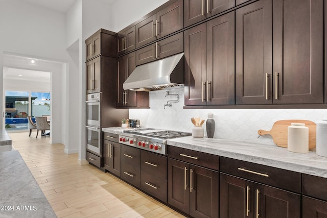 kitchen with dark brown cabinetry, under cabinet range hood, light wood-style floors, appliances with stainless steel finishes, and tasteful backsplash