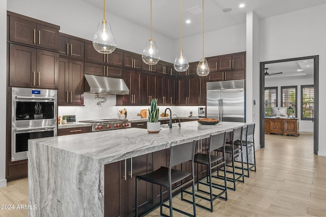 kitchen with appliances with stainless steel finishes, decorative backsplash, light wood-style flooring, and under cabinet range hood