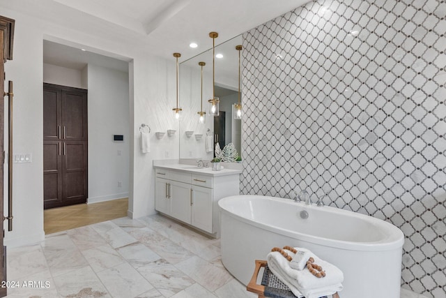 bathroom featuring marble finish floor, a freestanding tub, vanity, and baseboards