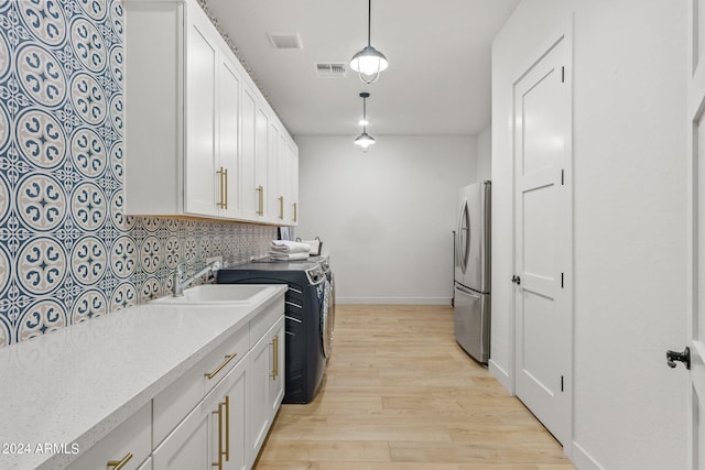 kitchen featuring a sink, visible vents, white cabinetry, freestanding refrigerator, and decorative backsplash