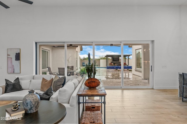 living area with light wood-style floors, a high ceiling, ceiling fan, and baseboards