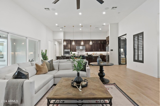 living room with light wood-style floors, visible vents, and a towering ceiling