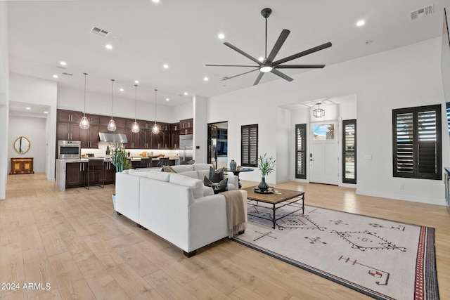 living room featuring a towering ceiling, light wood finished floors, visible vents, and recessed lighting