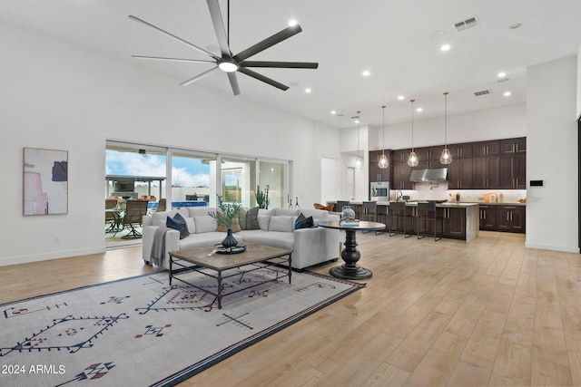 living area featuring light wood finished floors, baseboards, a high ceiling, and visible vents