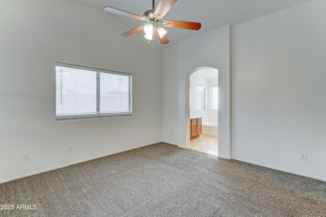 empty room with baseboards, ceiling fan, light carpet, a high ceiling, and arched walkways