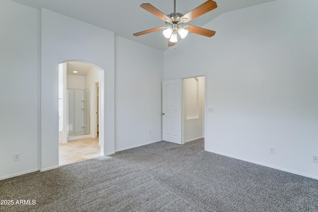 carpeted spare room featuring baseboards, arched walkways, and high vaulted ceiling