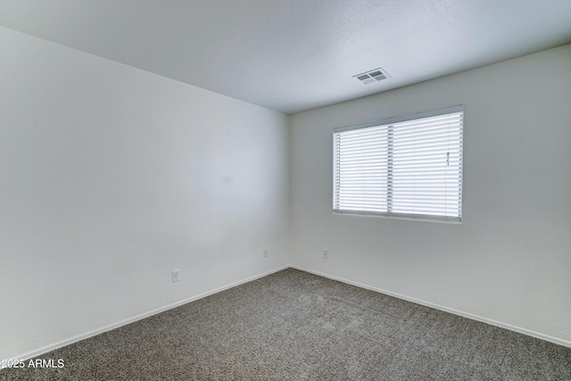 spare room featuring visible vents, dark carpet, and baseboards