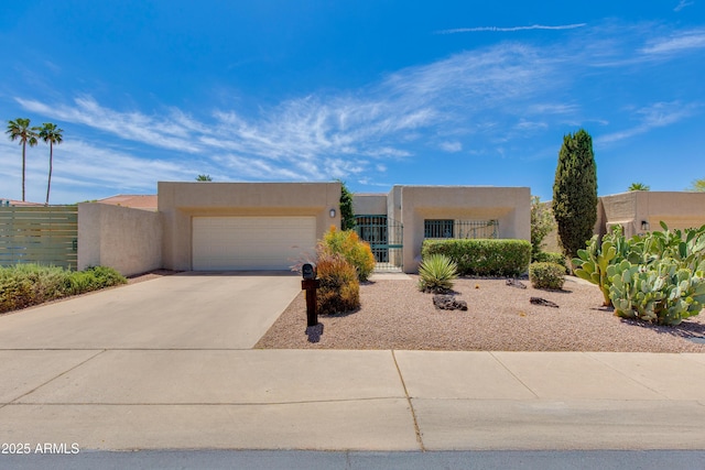 pueblo-style house with an attached garage, fence, driveway, and stucco siding