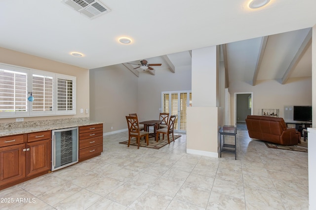 kitchen with wine cooler, brown cabinets, ceiling fan, light stone countertops, and open floor plan