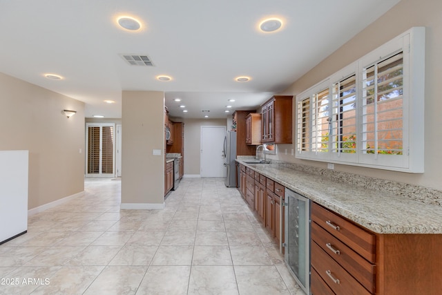 kitchen featuring wine cooler, freestanding refrigerator, a sink, light stone countertops, and recessed lighting