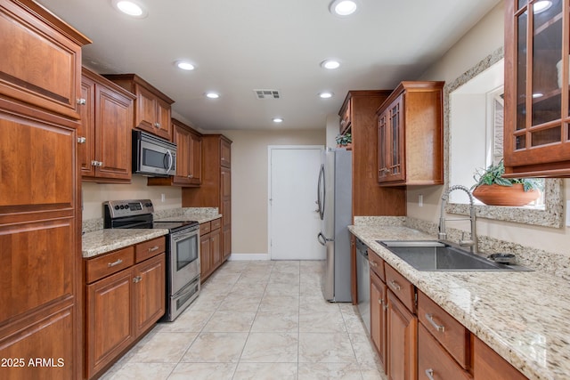 kitchen featuring appliances with stainless steel finishes, a sink, glass insert cabinets, brown cabinets, and recessed lighting