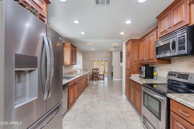 kitchen with appliances with stainless steel finishes, a sink, recessed lighting, brown cabinets, and light stone countertops