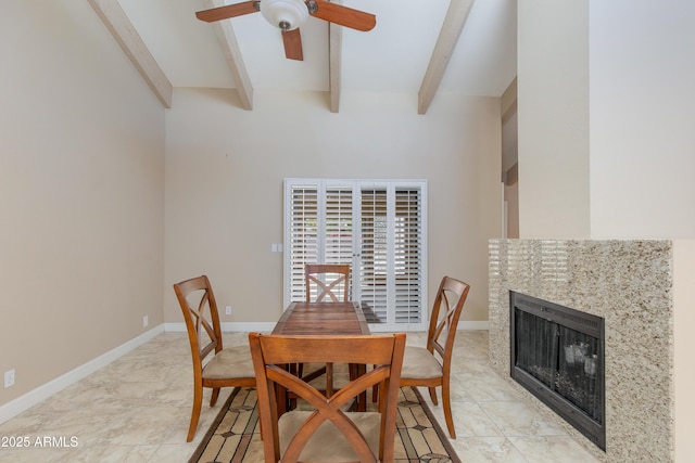 dining room with a ceiling fan, beam ceiling, a tiled fireplace, and baseboards