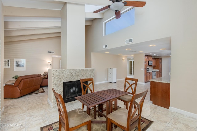 dining area featuring a ceiling fan, baseboards, a fireplace, high vaulted ceiling, and beam ceiling