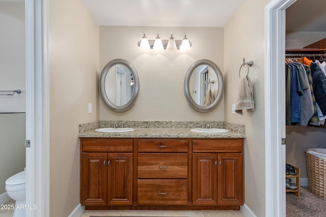 full bathroom with double vanity, baseboards, toilet, and a walk in closet