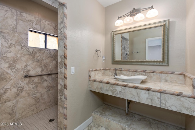 bathroom featuring a tile shower, a sink, and baseboards
