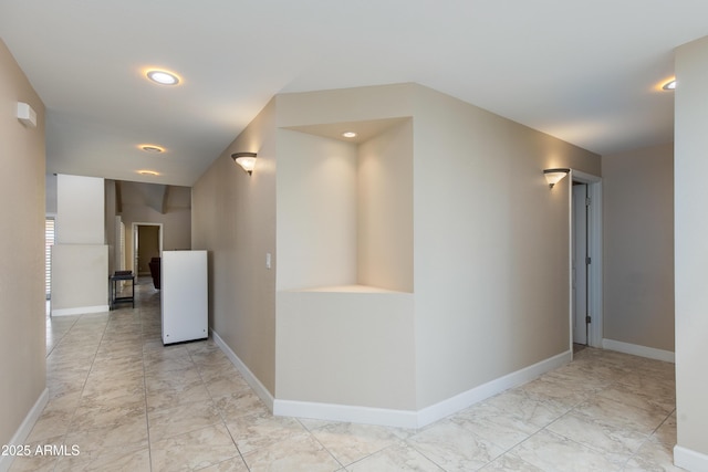 hallway featuring baseboards, recessed lighting, and light marble finish flooring