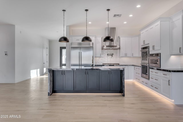 kitchen featuring appliances with stainless steel finishes, white cabinetry, a sink, and wall chimney exhaust hood