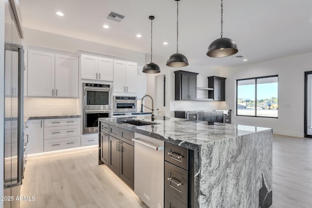 kitchen with appliances with stainless steel finishes, white cabinetry, decorative light fixtures, and an island with sink