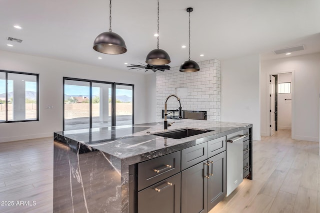 kitchen with a kitchen island with sink, a sink, visible vents, dark stone counters, and decorative light fixtures