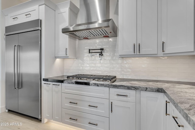 kitchen featuring stainless steel appliances, range hood, white cabinetry, and light stone countertops