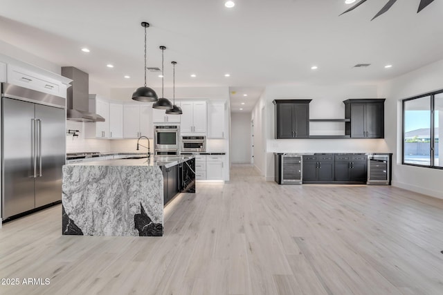 kitchen featuring wall chimney exhaust hood, white cabinetry, stainless steel appliances, and beverage cooler