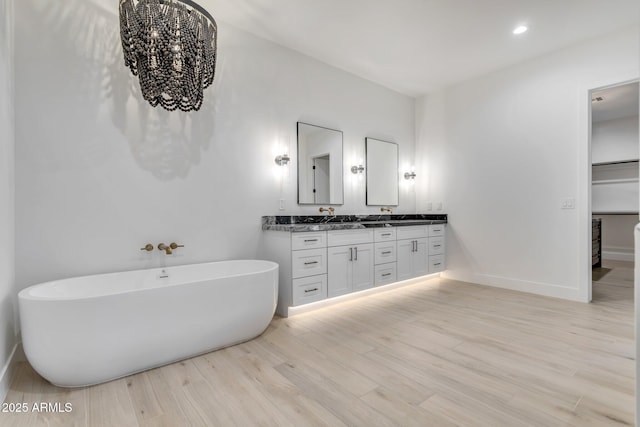 bathroom with double vanity, a freestanding tub, baseboards, and wood finished floors