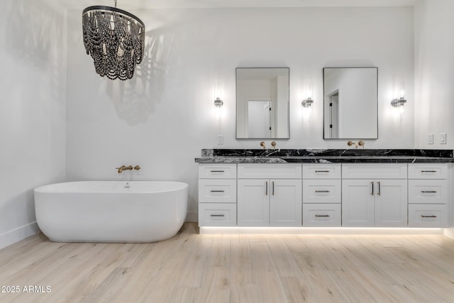 bathroom featuring double vanity, a freestanding bath, an inviting chandelier, and wood finished floors