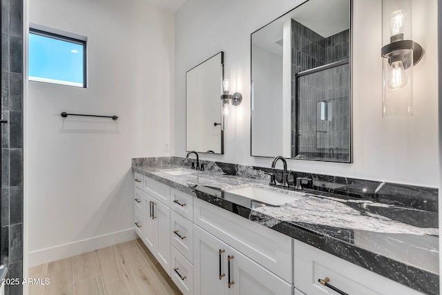 full bathroom with tiled shower, a sink, baseboards, and double vanity