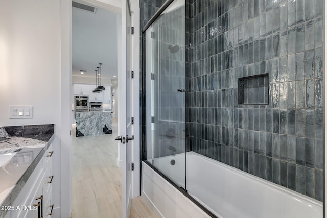 bathroom with wood finished floors, visible vents, vanity, and bath / shower combo with glass door